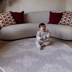 Baby girl sits on extra large round playmat a grey design looks like a rug but has the practical elements you need from a play mat textural batik effect and a subtle grey tone looks beautiful in modern interiors