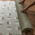 Hands unroll the double sided play mat with olive kilim and tan solstice designs perfect for play areas at home