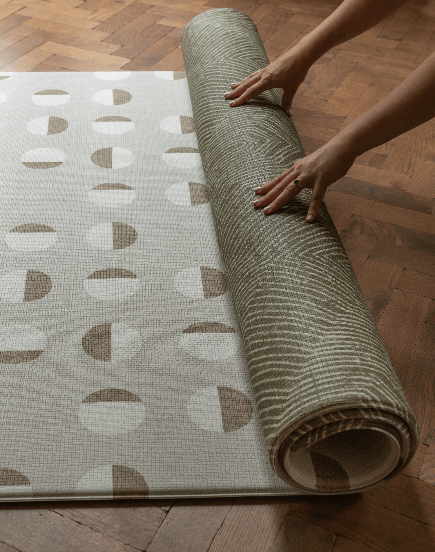 Hands unroll the double sided play mat with olive kilim and tan solstice designs perfect for play areas at home