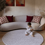 Baby girl sits comfortably on the extra large round padded playmat by totter and tumble with an animal print design to complement and add texture into stylish family homes