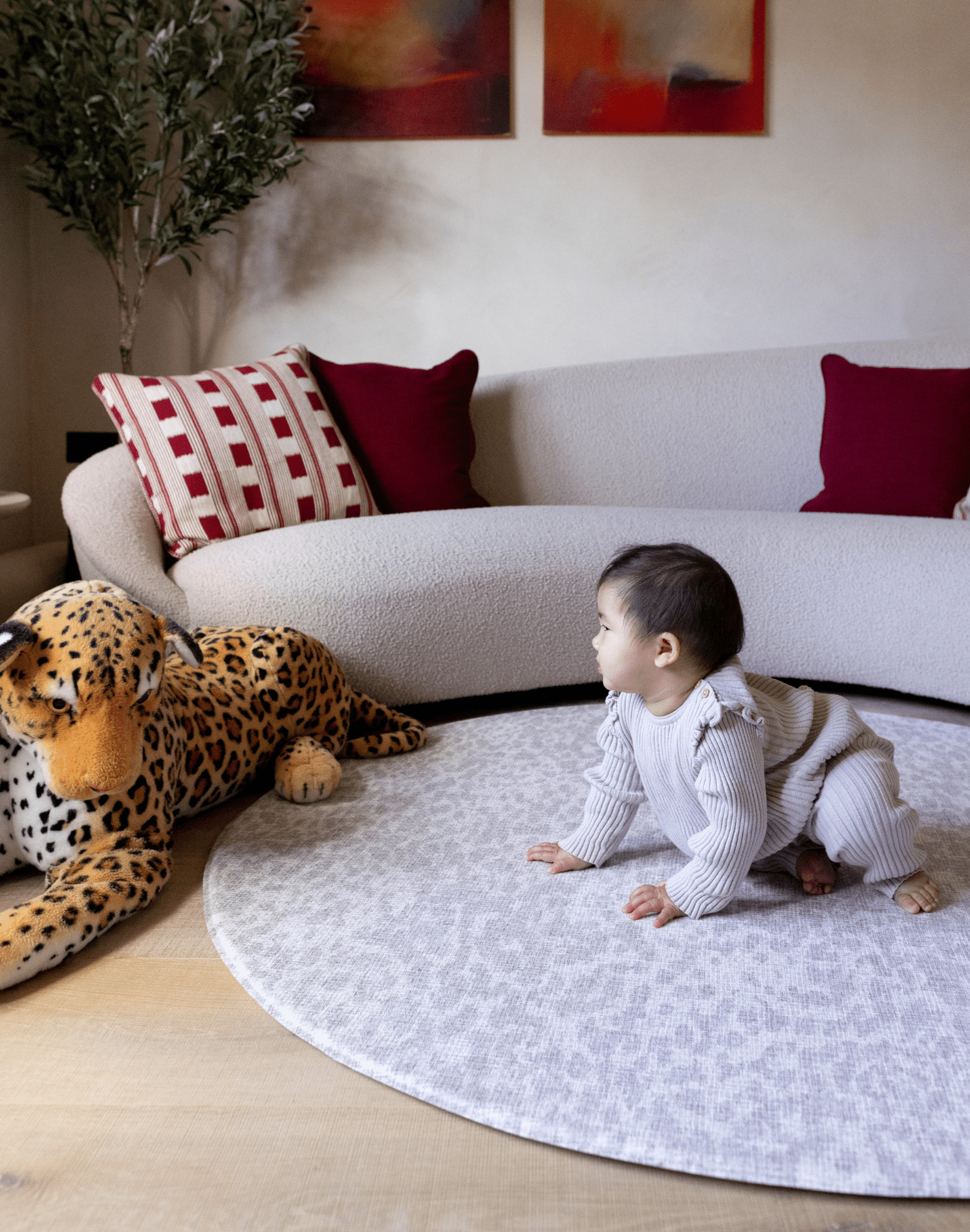 Baby girl sits on the large round playmat the sunda with a delicate leopard print design that complements modern living space the little girl gazes at a large leopard soft toy