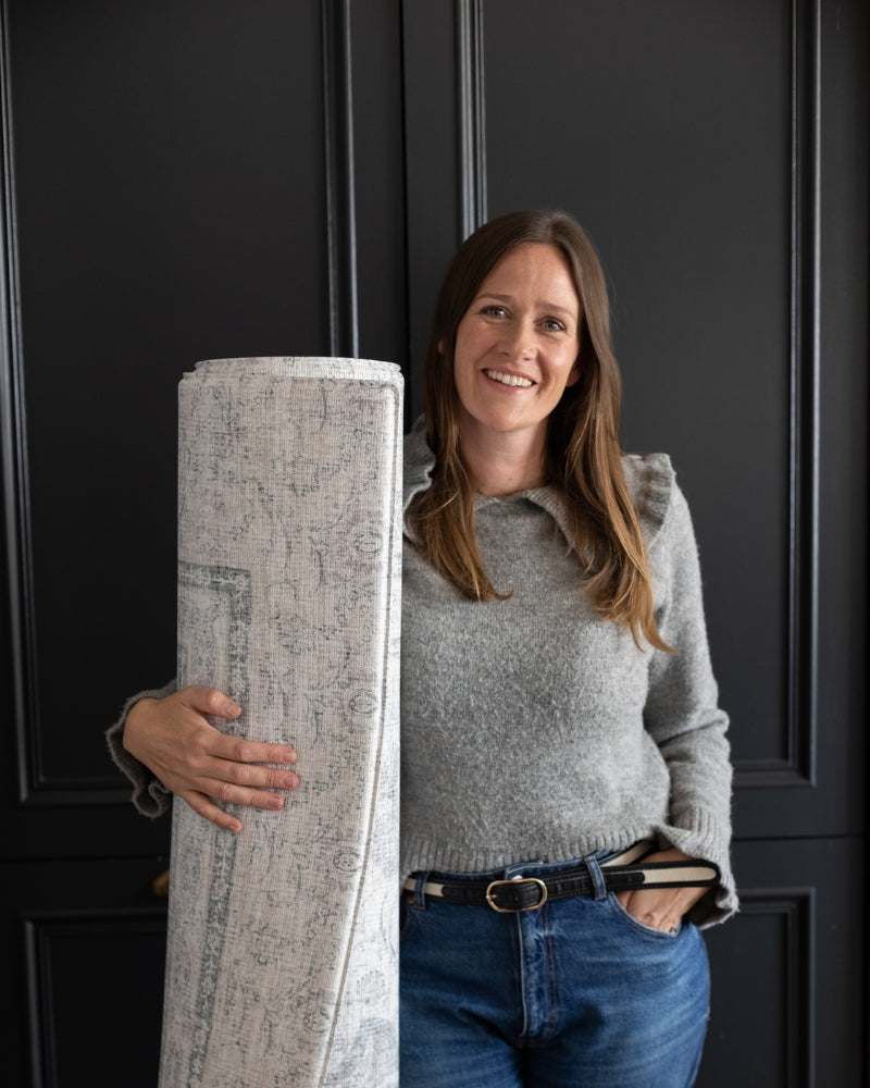Susie Stubbs, founder of Totter + Tumble holding a large rolled grey playmat