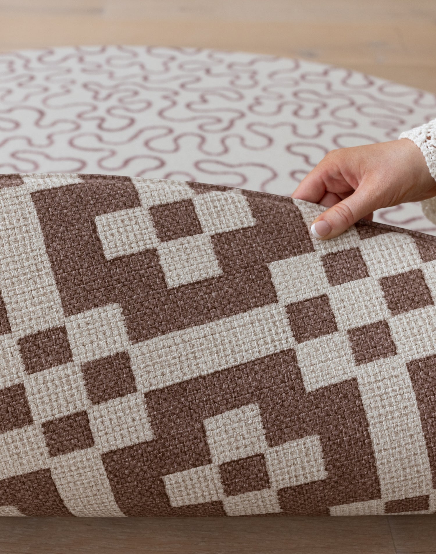 A hand folds over a Totter + Tumble reversible baby mat, revealing a hexagon play mat design in brown on the reverse.