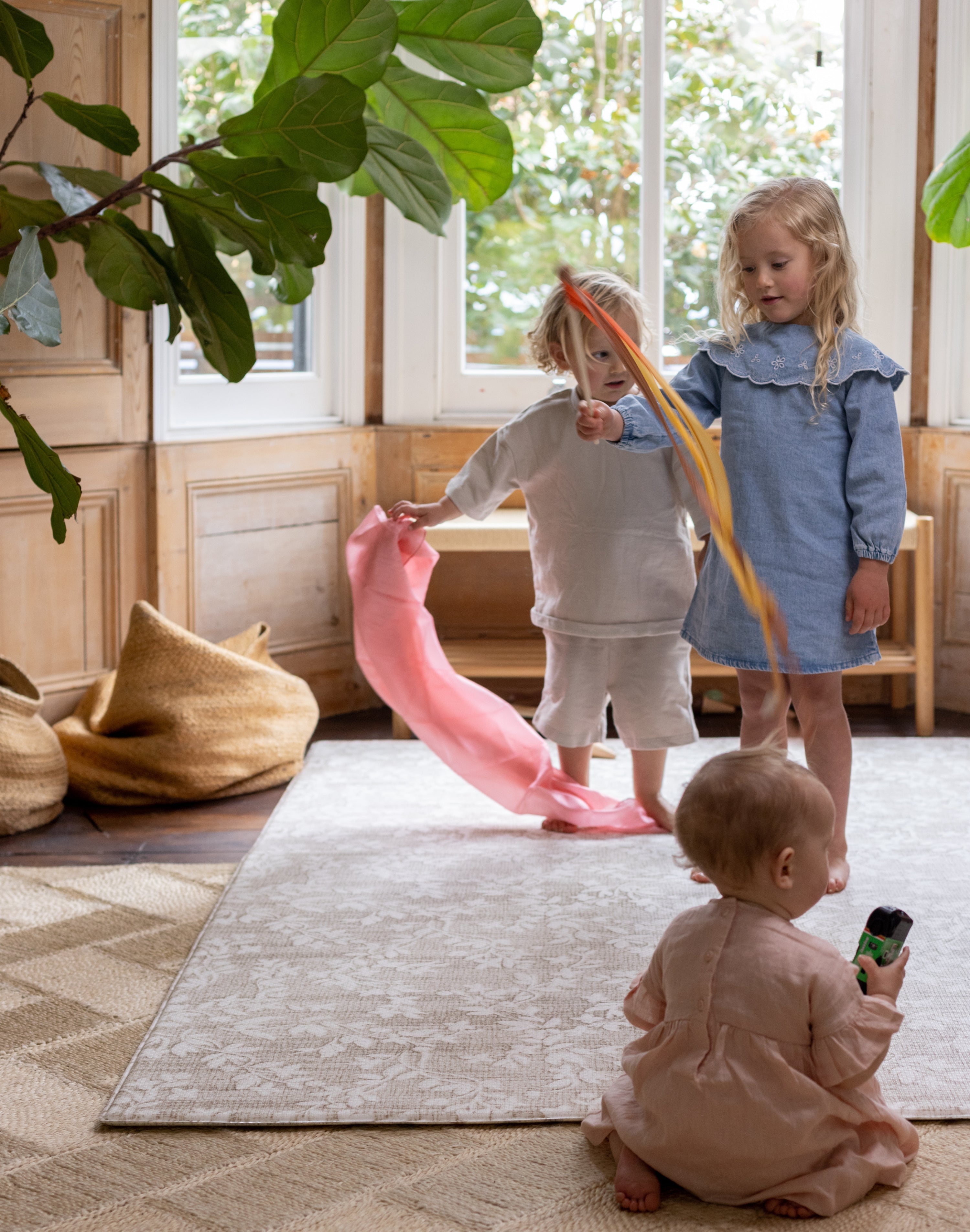 Three children playing with colorful ribbons on a designer baby play mat that matches home decor