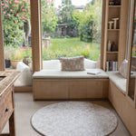 Cozy reading nook with a window seat, cushions, and a round minimalist baby play mat