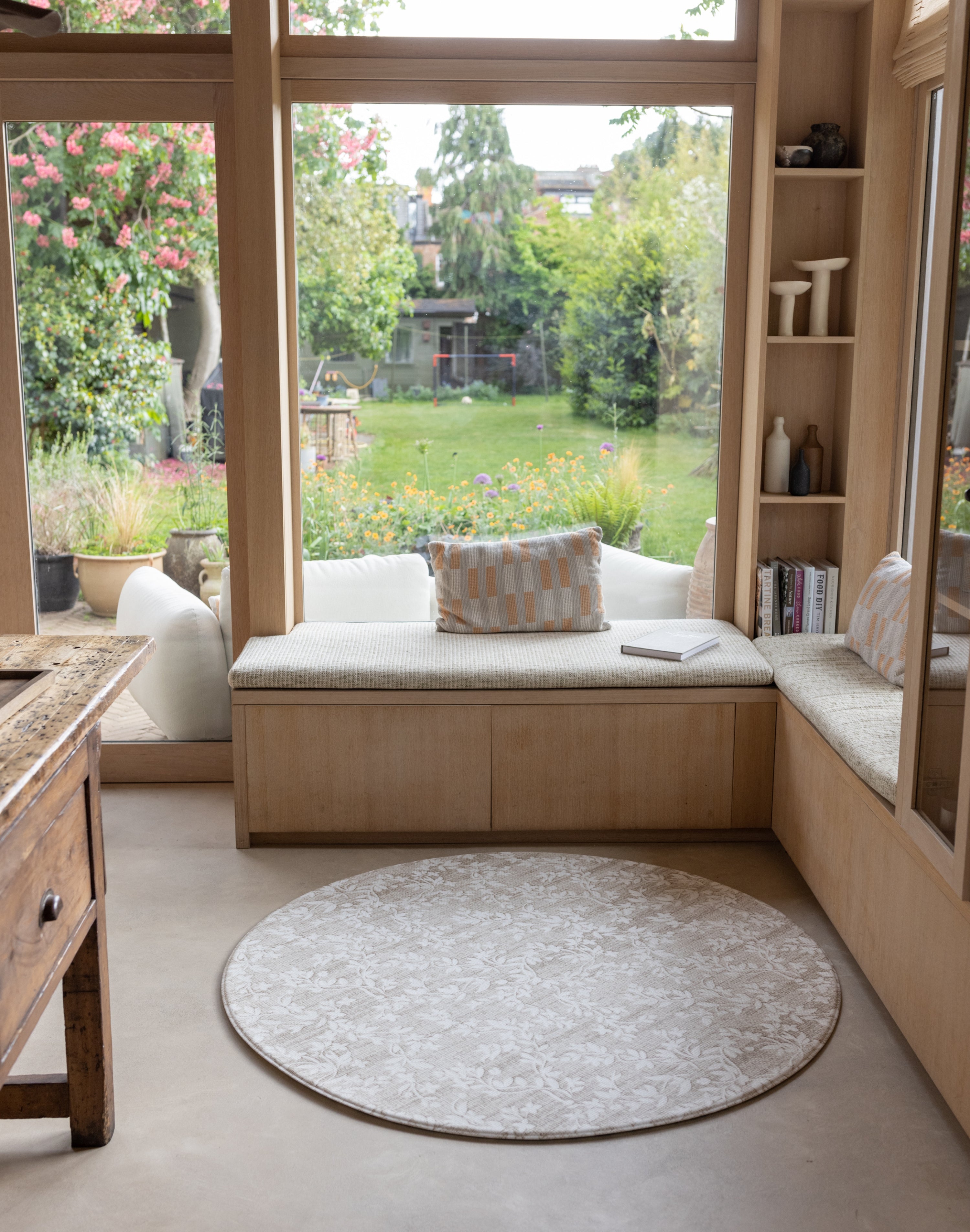 Cozy reading nook with a window seat, cushions, and a round minimalist baby play mat