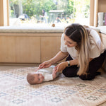 Woman playing with a baby on a neutral luxury play mat for tummy time