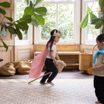 Child in a pink cape and crown playing with a toy horse in a room with an aesthetically pleasing baby play mat