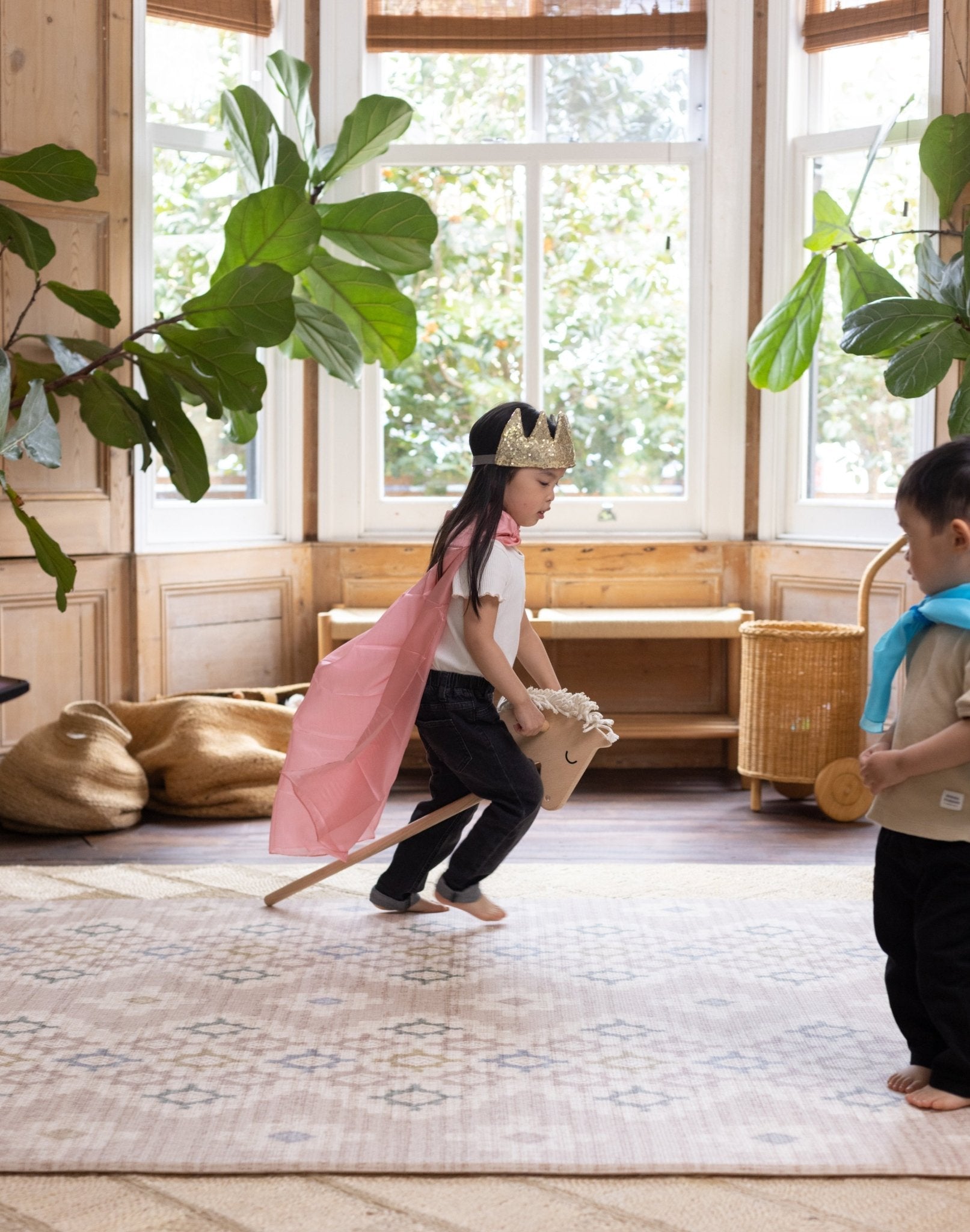Child in a pink cape and crown playing with a toy horse in a room with an aesthetically pleasing baby play mat
