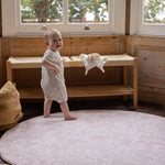 Baby standing on a thick luxury padded foam round pink rug in a modern stylish room 