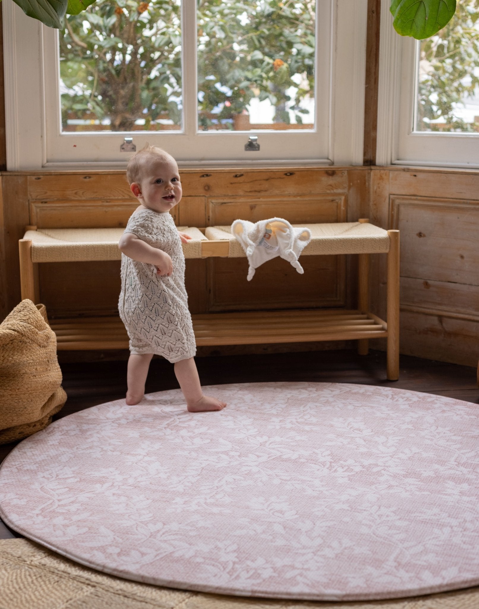 Baby standing on a thick luxury padded foam round pink rug in a modern stylish room 