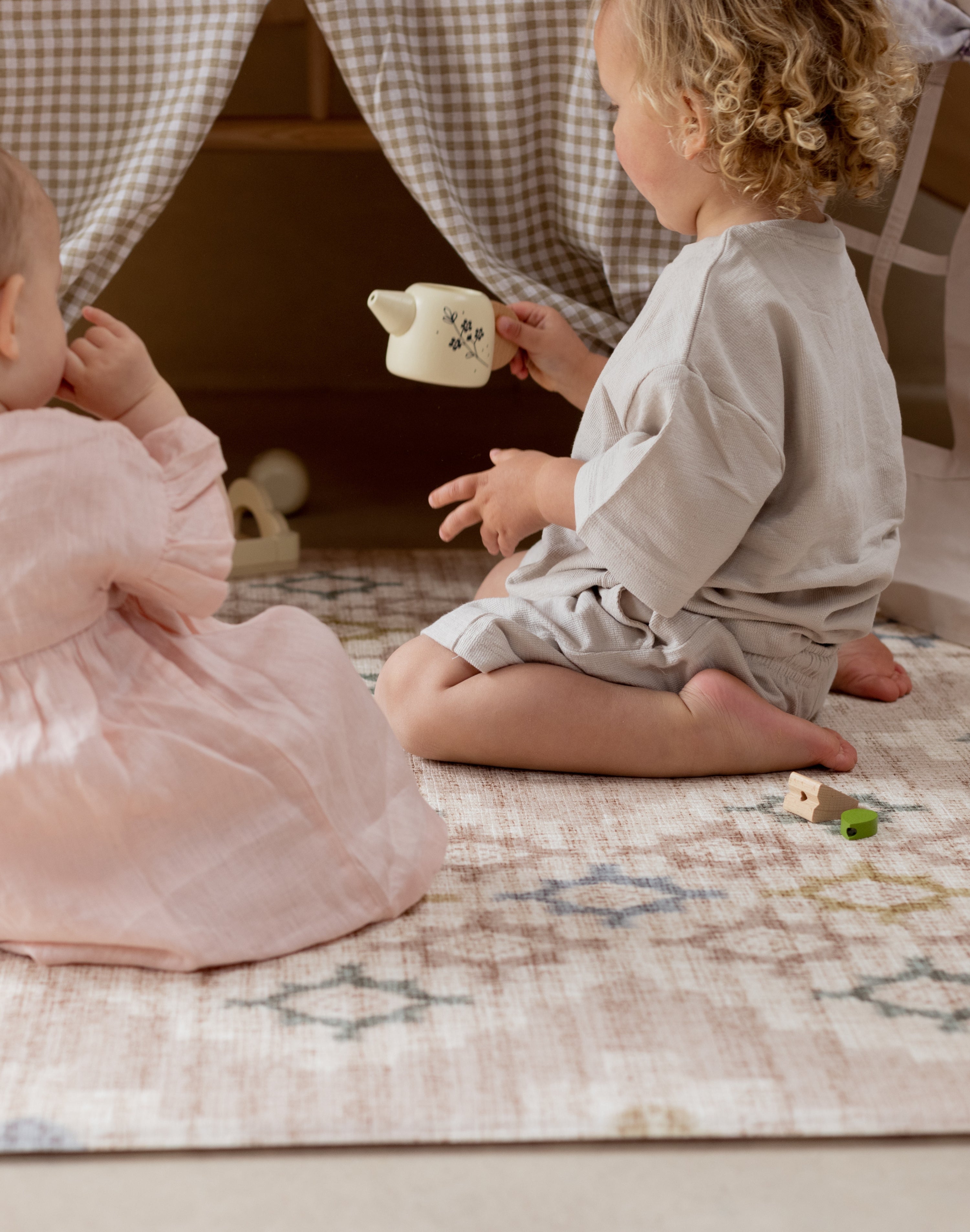 Two children playing with a tea cup on a reversible baby play mat with elegant design