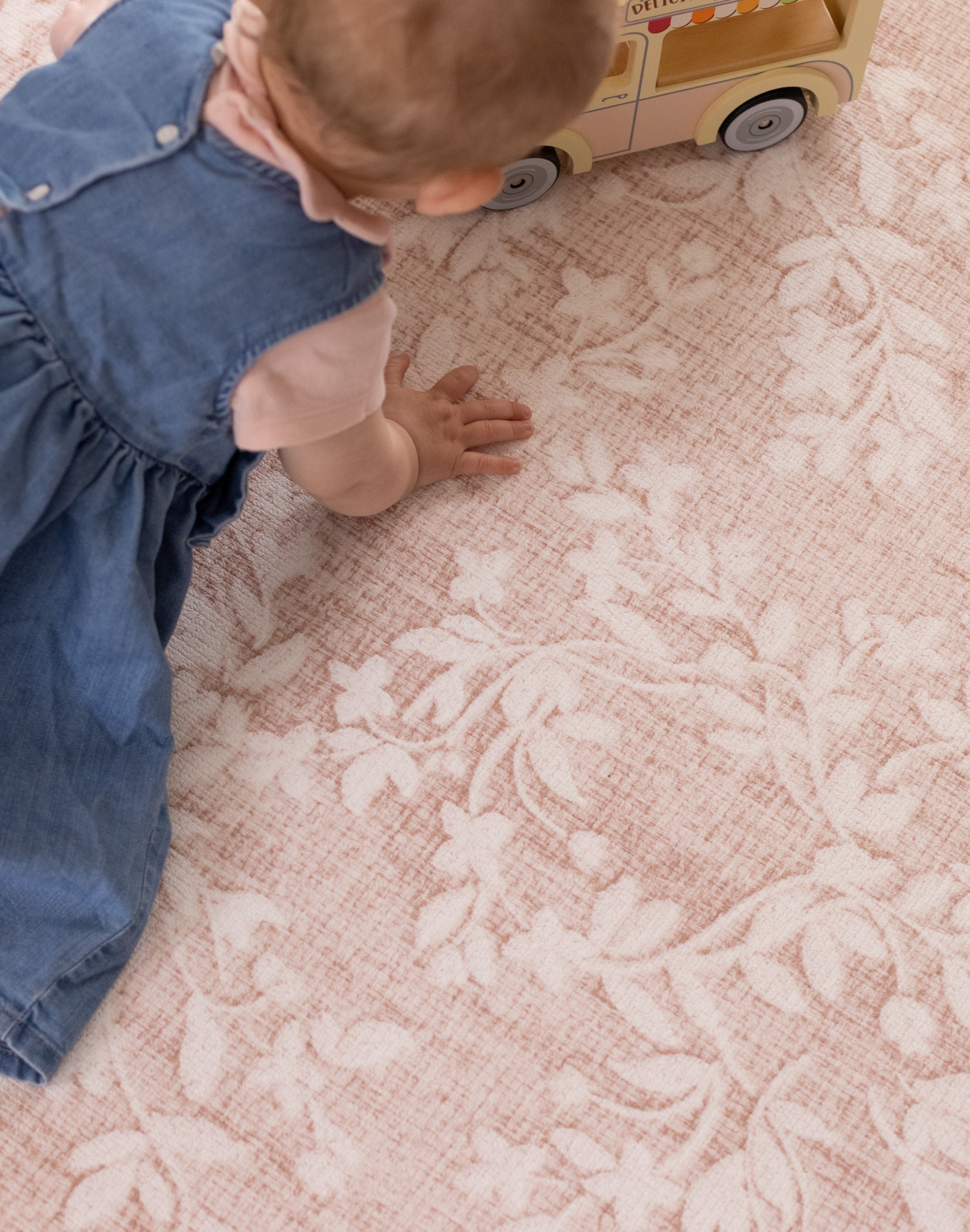Child playing with a wooden toy on a pink modern and cushioned mat for baby learning to crawl