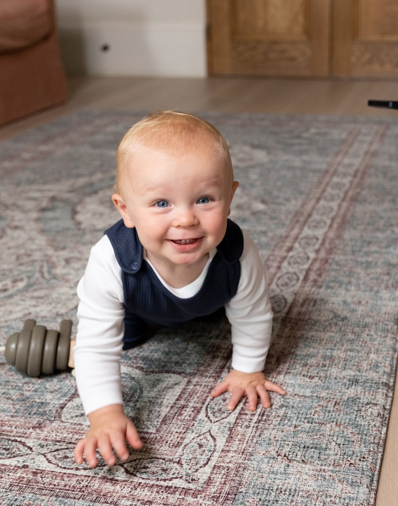 Smiling toddler crawling on Totter + Tumble playmat enjoying safe playtime.