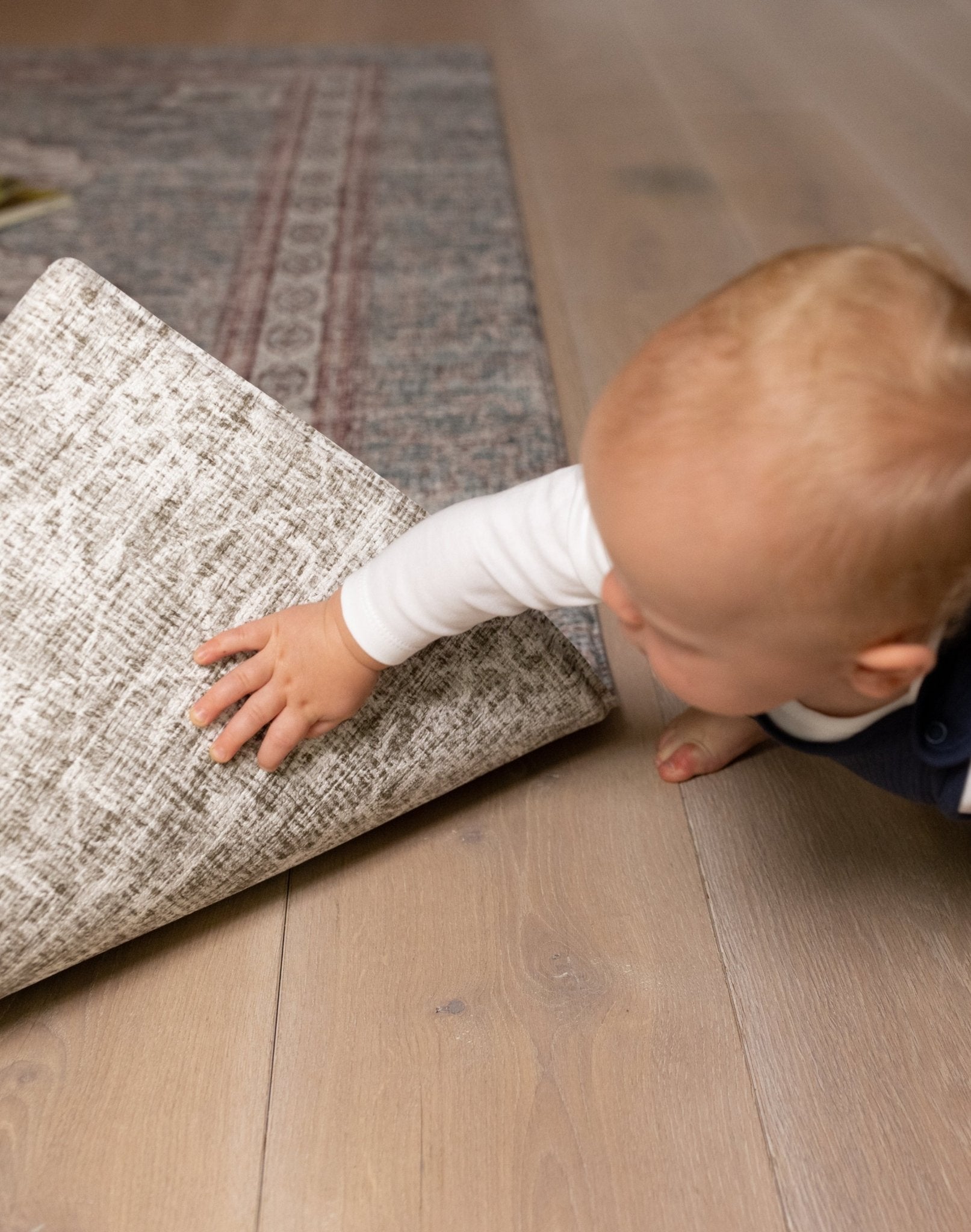 Baby lifting edge of Totter + Tumble playmat showing non-slip backing and a new design on the reverse