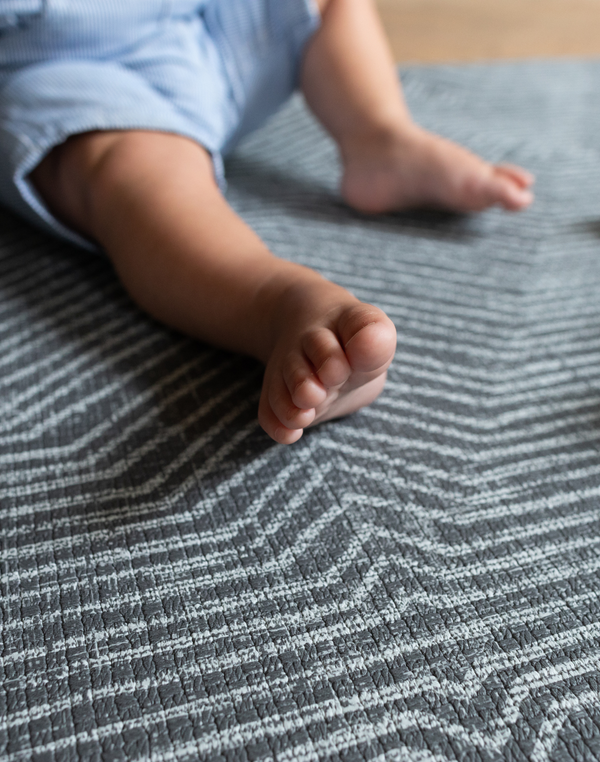 Baby feet are supported on the grijs speelmat designed from birth to keep floor play protected and safe 