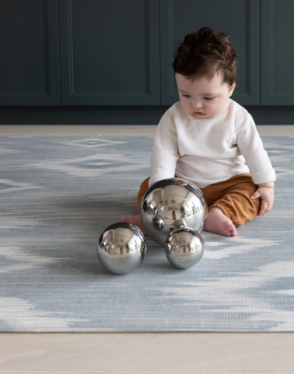 Baby playing with sensory metallic balls on Light blue and beige play mat with subtle diamond design inspired by ikat motifs ideal for family living spaces