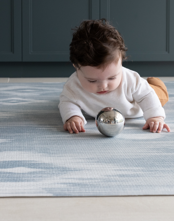 Baby playing with sensory toy on A practical playroom rug The Totter and Tumble play mats have a wipeable surface so you can keep your home clean and tidy and it can look stylish as well 