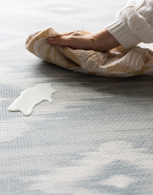 Milk spill being wipe away on Atlas blue and beige tumbling mat by totter and tumble for easy cleaning in the home