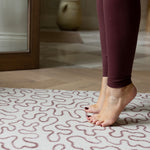 Person wearing maroon leggings stepping onto a patterned rug-like mat in a home setting for yoga or exercise.