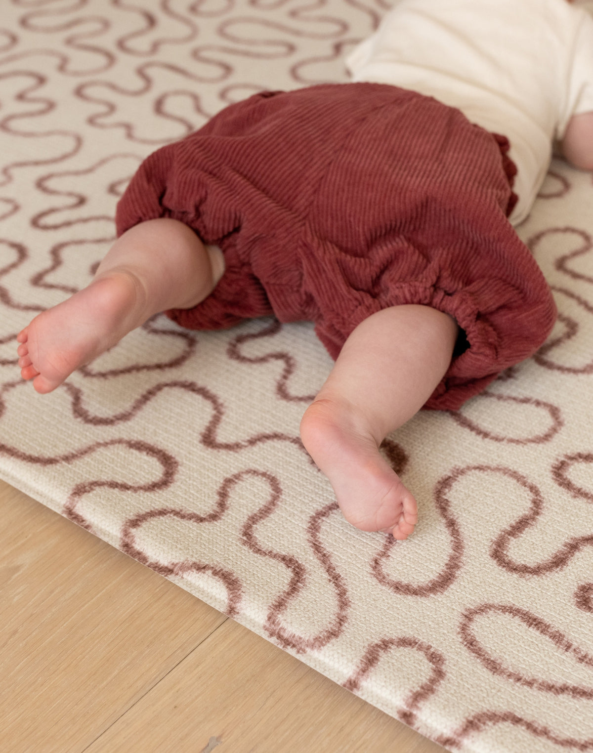 Baby on The Brecon play mat, a soft, earthy tone crawling mat with a hiking trail motif inspired by Welsh heritage.