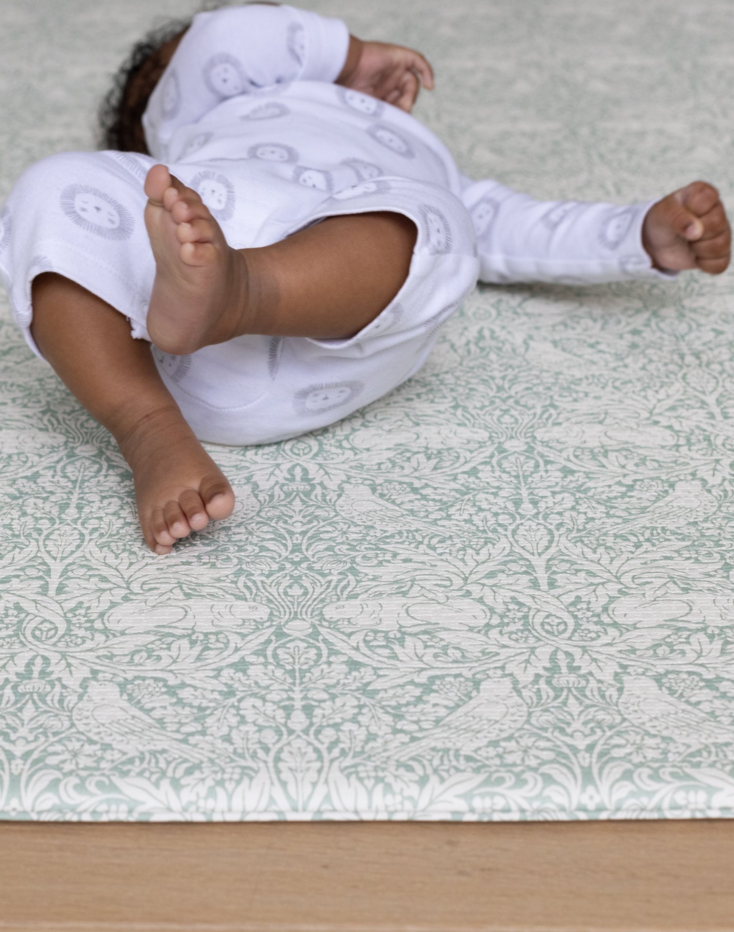 Little baby feet on a soft playmat in a subtle sage green William Morris design.