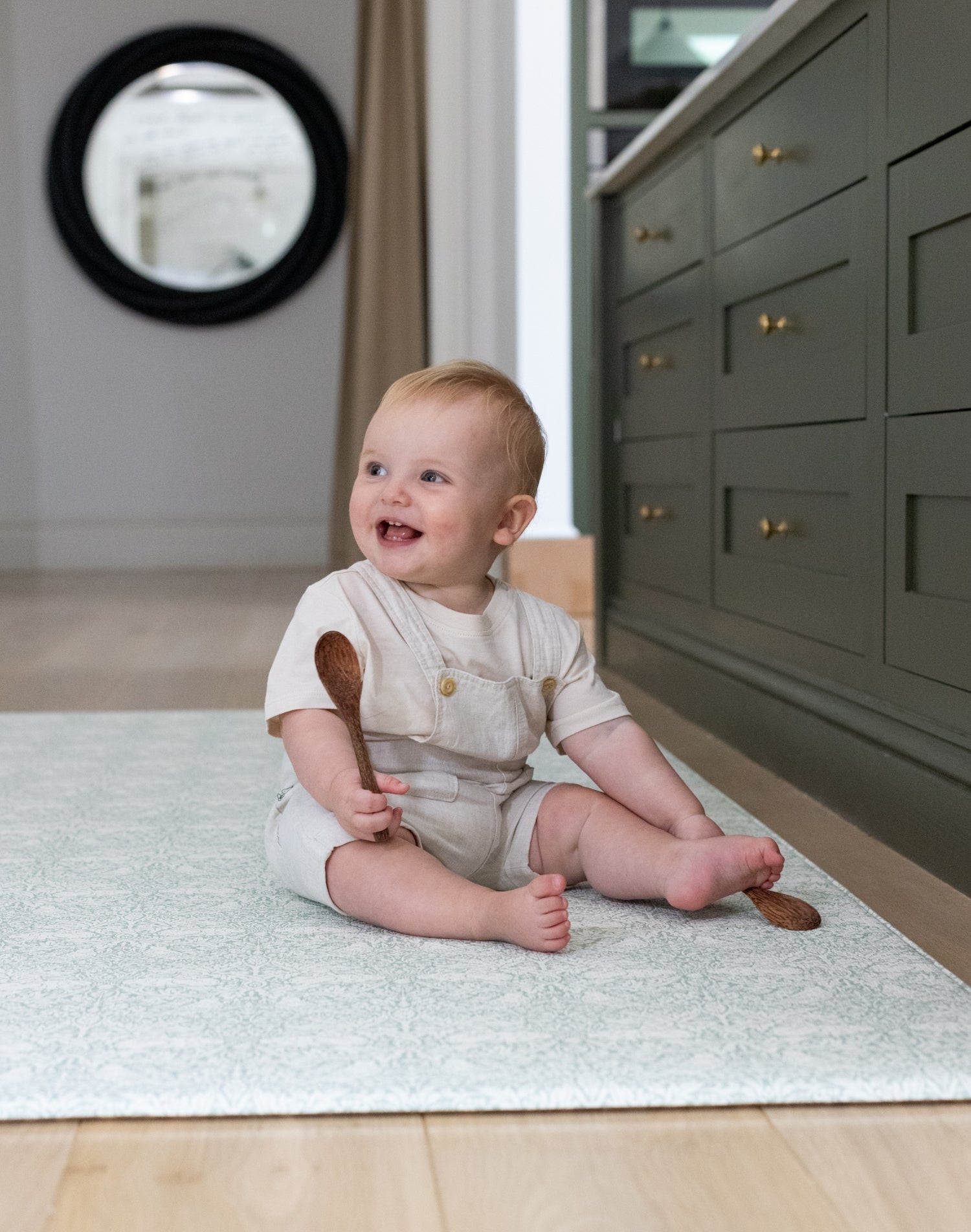 Toddler sits comfortably on The Brer Rabbit Playmat in the kitchen. The playmat is a stylish baby essential that blends designer nursery decor with practical, non-toxic materials.