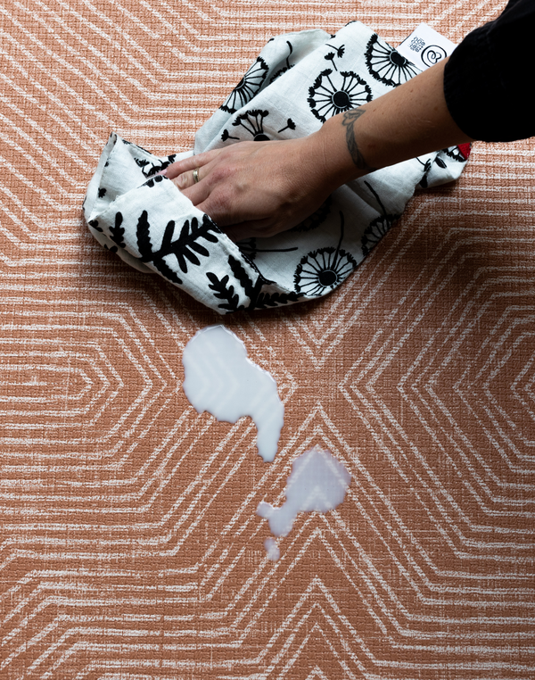 Parents using soft cloth to wipe spilled milk off sealed, waterproof totter and tumble play mats