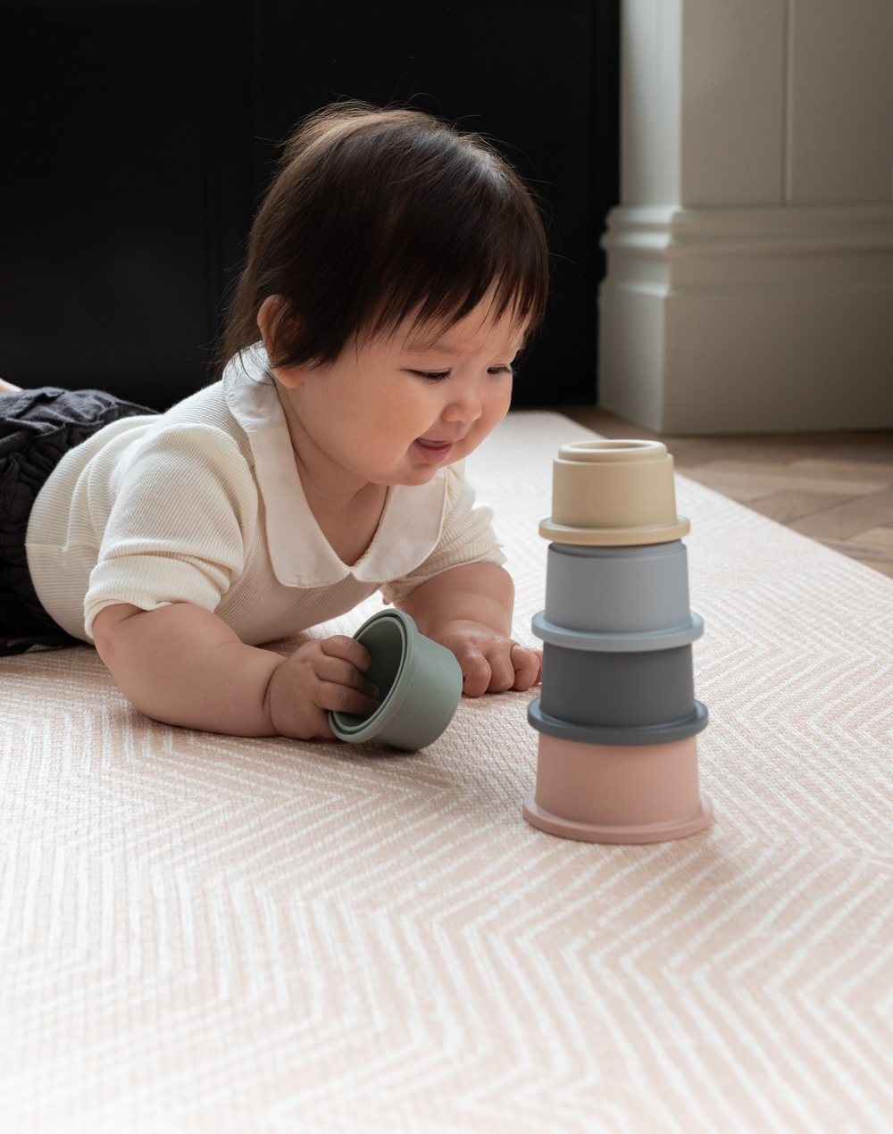 Little girl enjoys floor play with stacking cups on roze speelmat with gentle kilim textile design 
