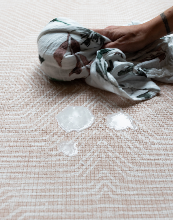 Wiping up milk with muslin on waterproof baby playmat 
