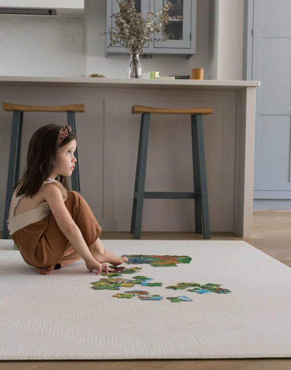 Child puts together a puzzle on the neutral Globe Trotter baby play mat that sits stylishly in a modern kitchen