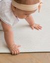 Little girl crawls across the Globe Trotter neutral play mat with a spongy surface that protects on hard wood flooring 