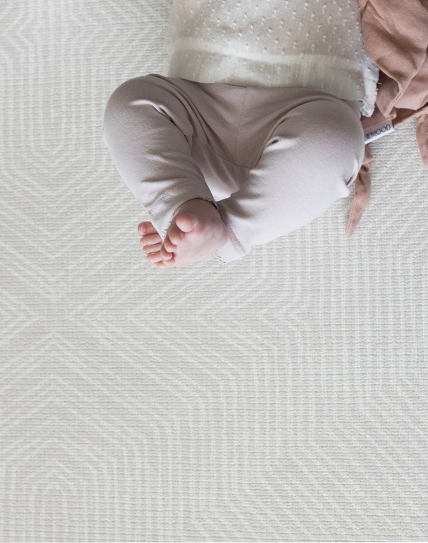 A baby lays on their back on the Globe Trotter play rug designed to look like a textile rug to keep your home stylish while providing comfort for babies on the floor