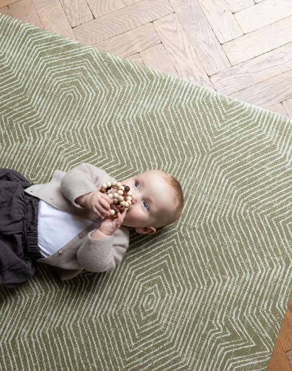 Baby is supported during play on the olive green play mat by Totter and Tumble with a decorative kilim effect 
