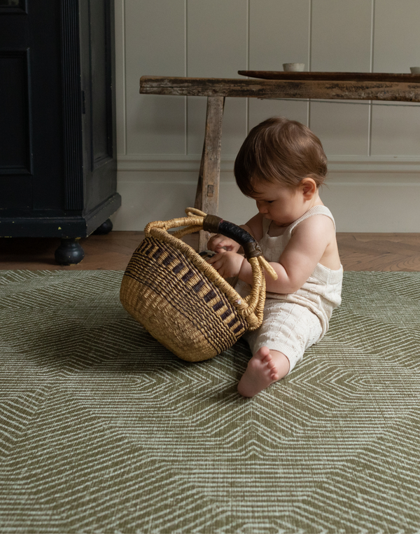 Baby plays with a basket sitting on the Harvester green baby mat that looks stylish in modern homes 