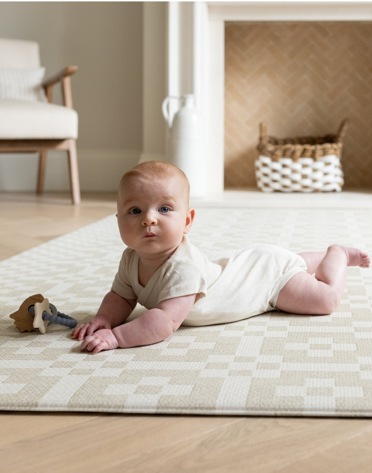 Baby on The Holbein, a calming colour play mat with a Portcullis motif in stone and chalk for tummy time and play.