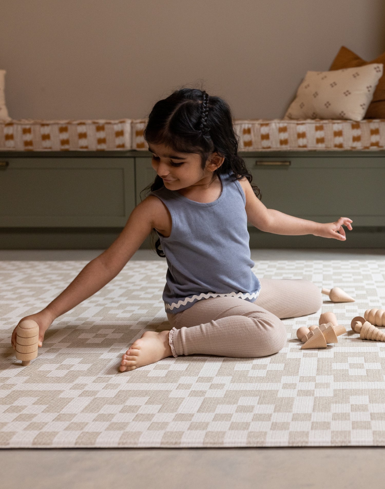 A girl plays on The Holbein, a large baby playmat for toddlers with a heritage-inspired, Welsh tapestry pattern.