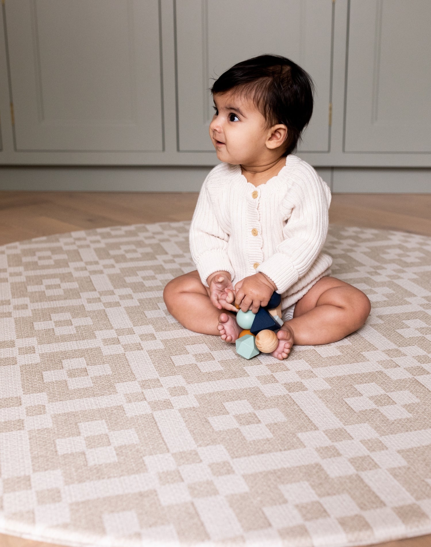 Toddler sits quietly on The Holbein, a muted beige playmat designed for comfort, play, and peaceful moments.