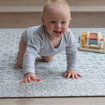 Smiling baby crawling on stylish grey playmat with colourful blocks