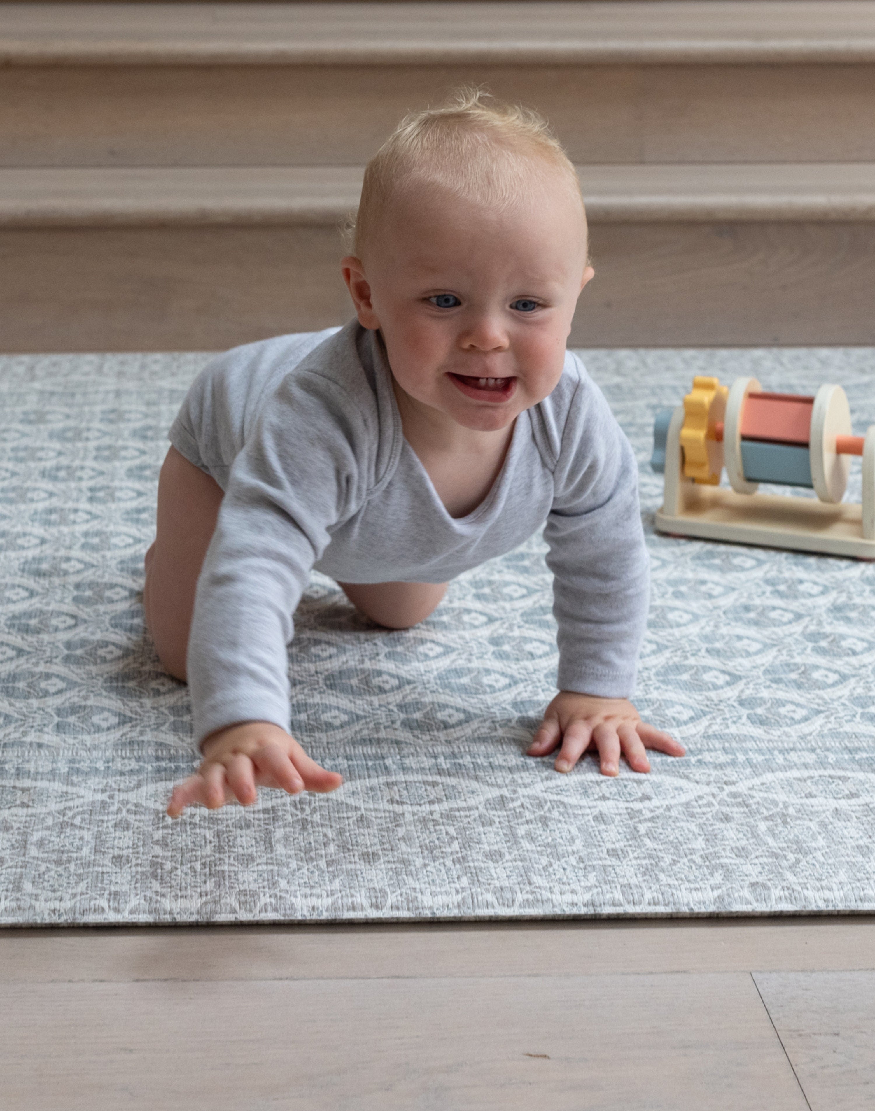 Smiling baby crawling on stylish grey playmat with colourful blocks