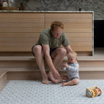 Parent and baby sitting together on large grey and blue playmat