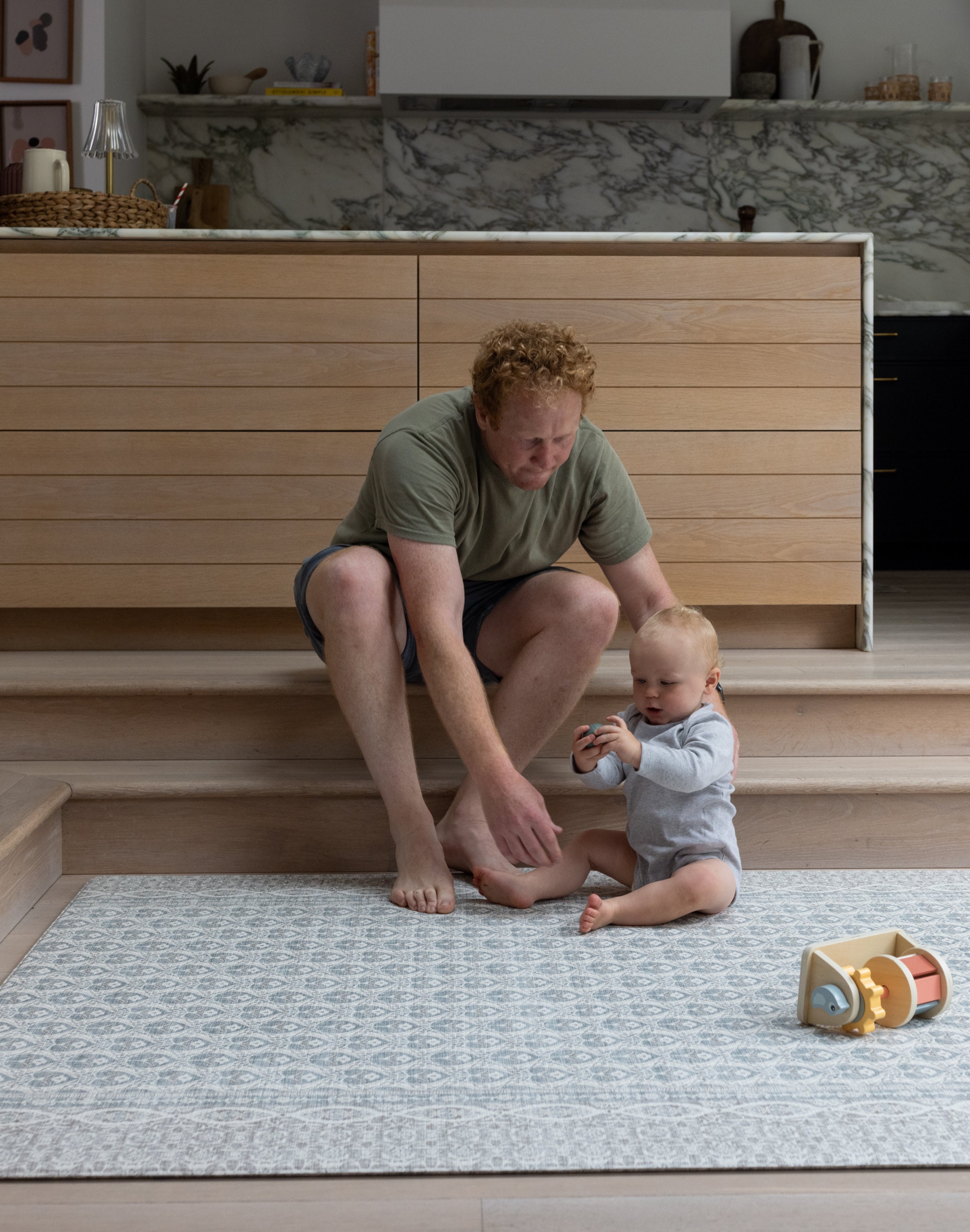 Parent and baby sitting together on large grey and blue playmat