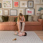 A mum sitting on a couch with a child on the floor in a living room with a large play mat