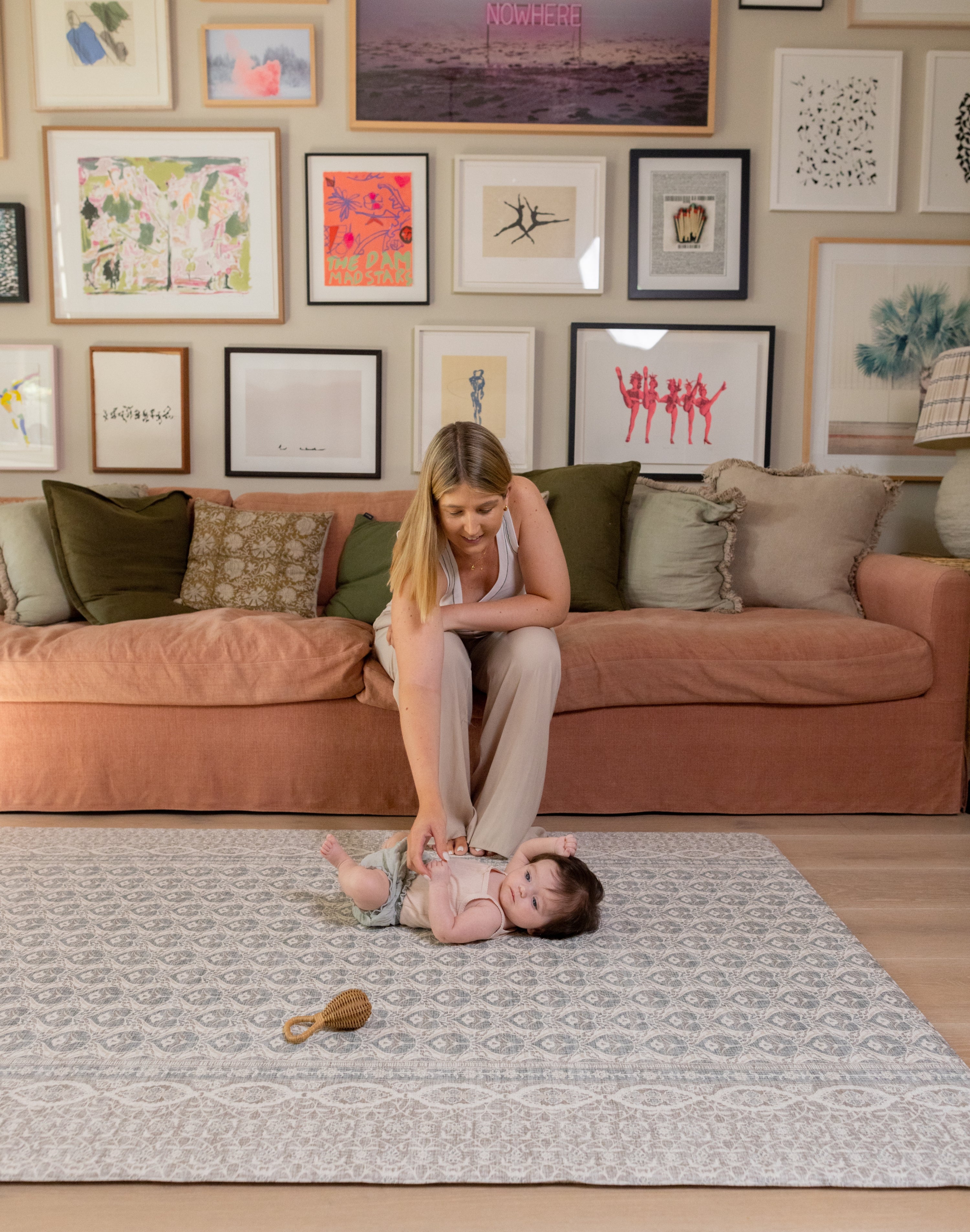 A mum sitting on a couch with a child on the floor in a living room with a large play mat