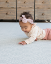 Baby with headband lays on protective play mat with modern scalloped design in gentle blue tones 
