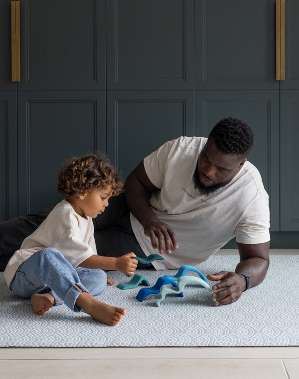 Man and boy playing on scalloped Mariner design play mat keeping comfortable on the memory foam and enjoying open play wooden toys 