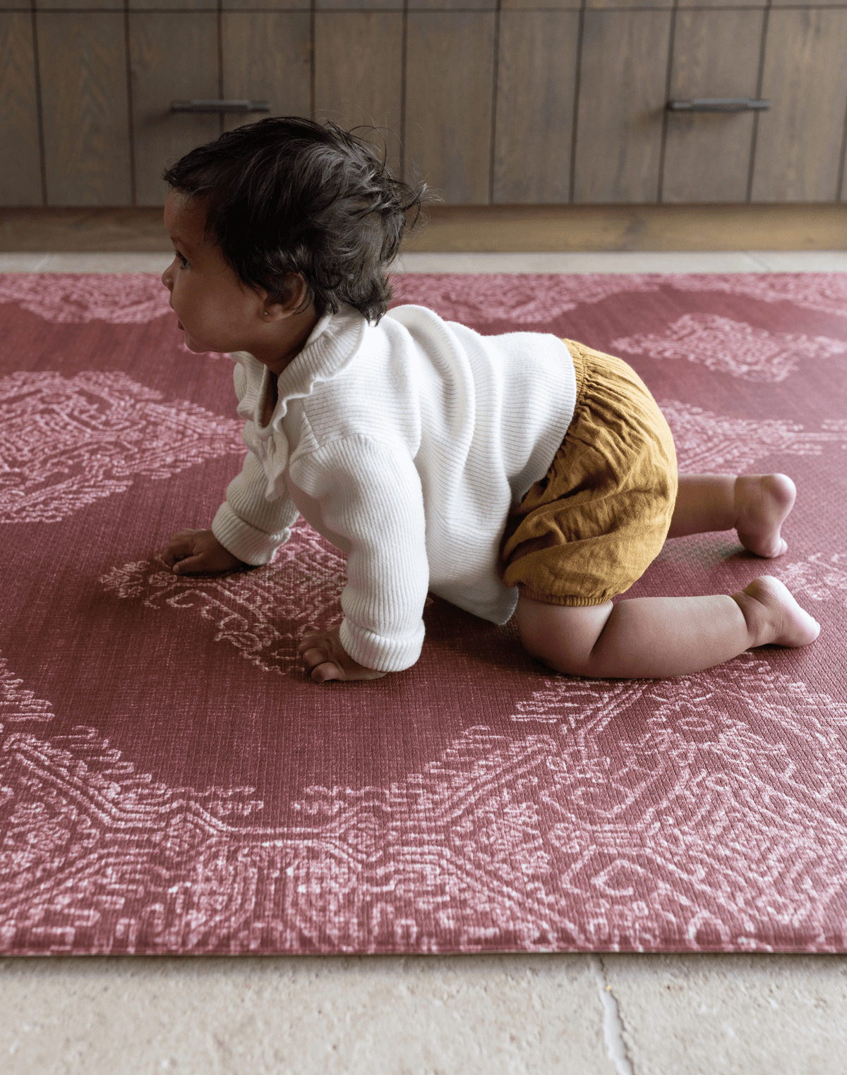 Baby crawls across large playing mat with thick memory foam to support joints and a textured surface for traction and support the red color complements boho kitchen styling 