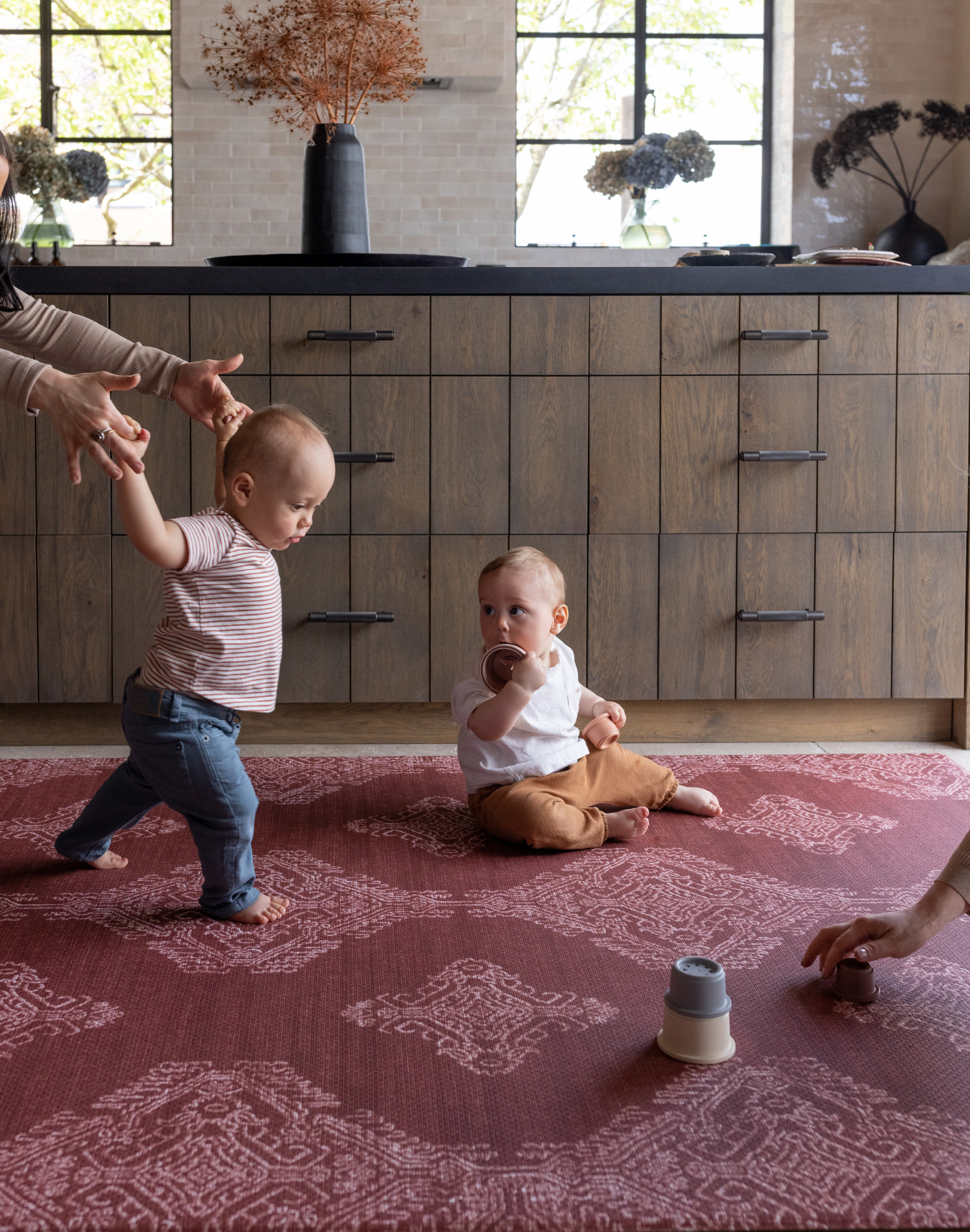 Padded large playmat in vibrant red design in kitchen with babies and their mother enjoying floortime play in comfort
