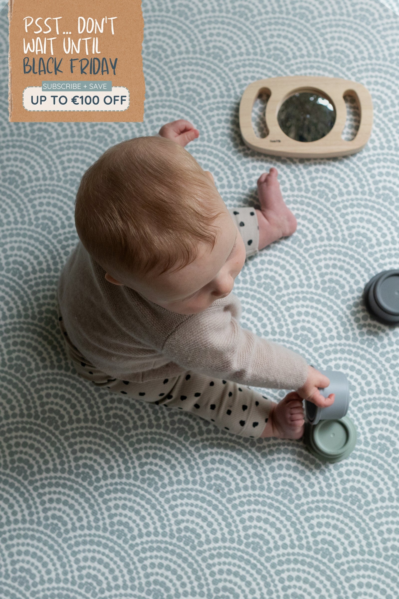 Sign that reads Don't wait until Black Friday for up to €100 off playmats. Overhead picture of a child playing on a soft patterned crawling mat.