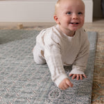 Baby crawling on a cushioned playmat with a Persian rug design